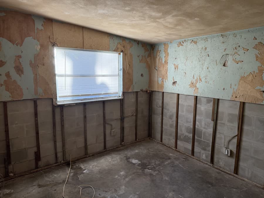Room with wet drywall cut out to the studs and old wallpaper peeling