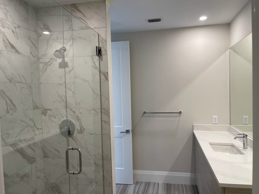 Glass shower with marble look porcelain tile and a vanity