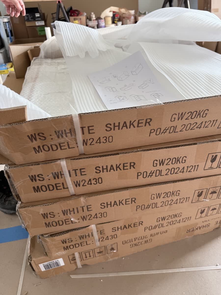 Boxed white shaker cabinets stacked on a protected floor