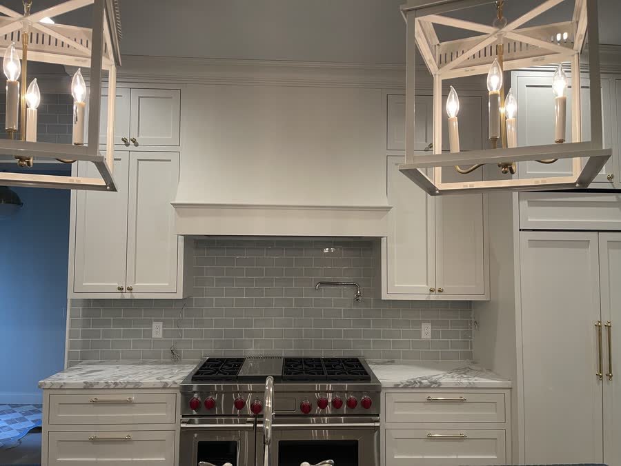 White shaker kitchen with lantern pendants, a glass tile backsplash, a pro range and a paneled refrigerator