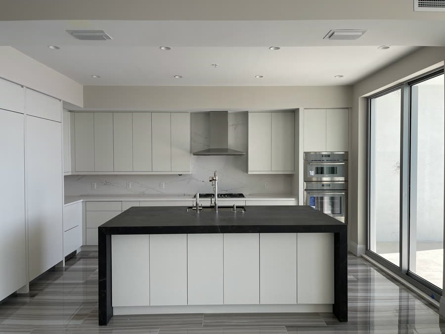 Modern white flat panel kitchen with a black waterfall island and stainless hood