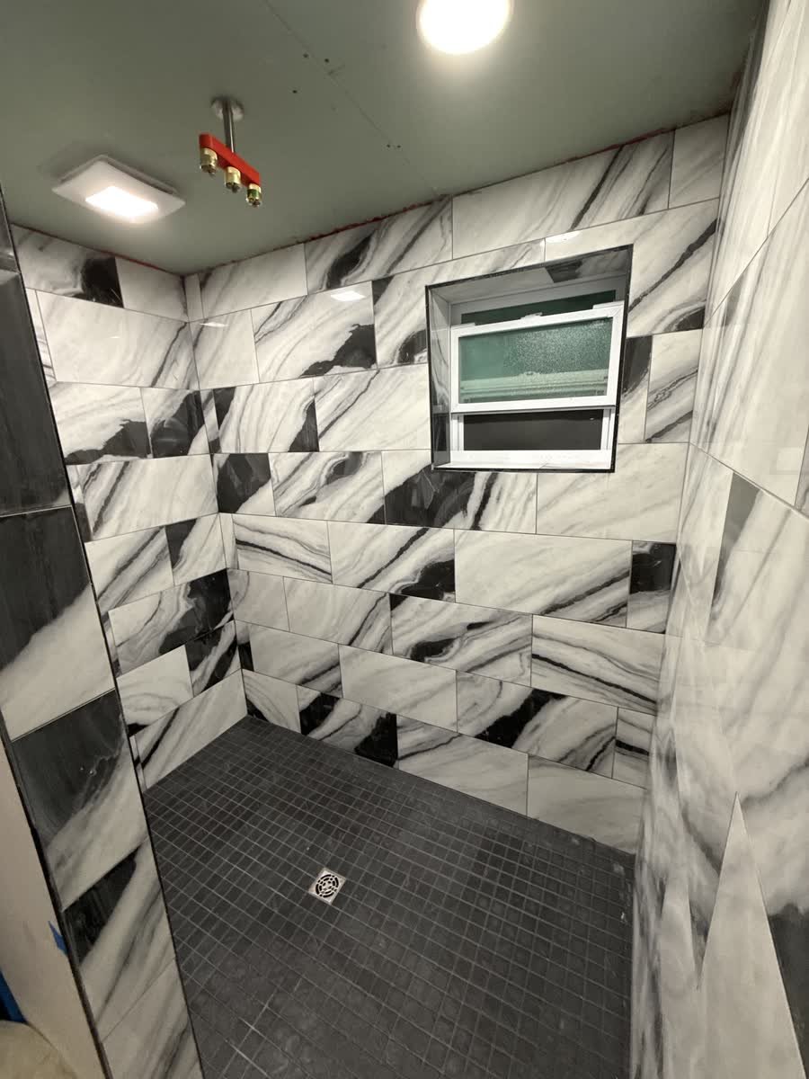 Walk-in shower with large black and white graphic tile and a black mosaic floor