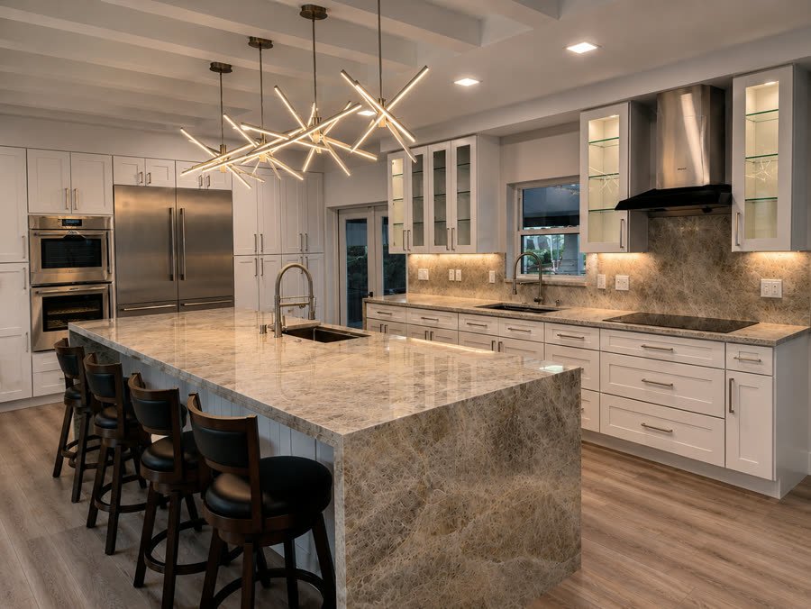 White kitchen remodel with a quartzite waterfall island, four bar stools and brass starburst pendants